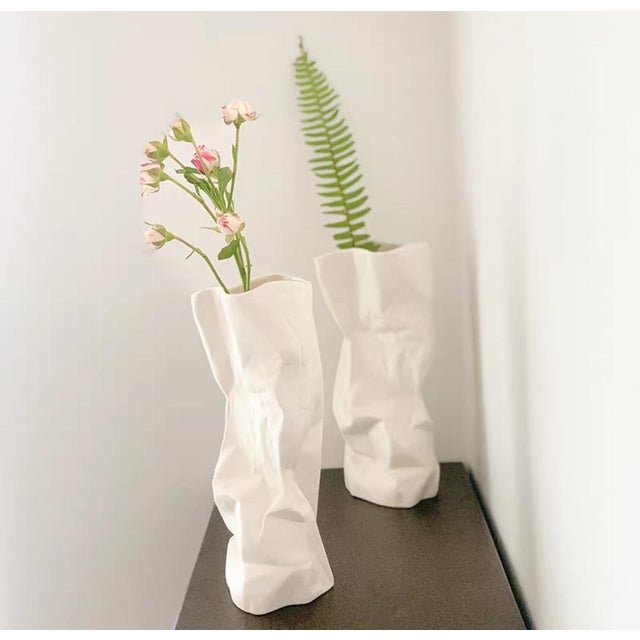 A pair of white ceramic vases, designed in a unique pleated paper bag shape, with a soft antique texture on the surface....