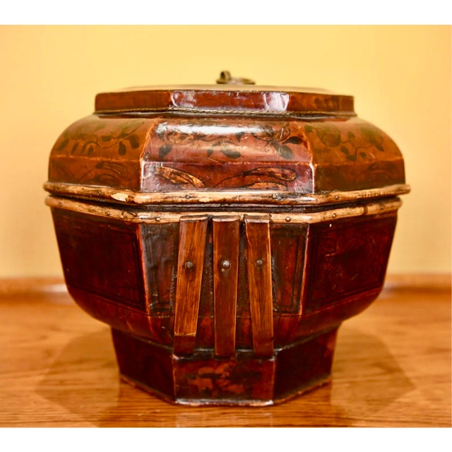 An antique Chinese wooden lidded storage vessel in a deep reddish-brown lacquer and decorated with faded black and gilt...
