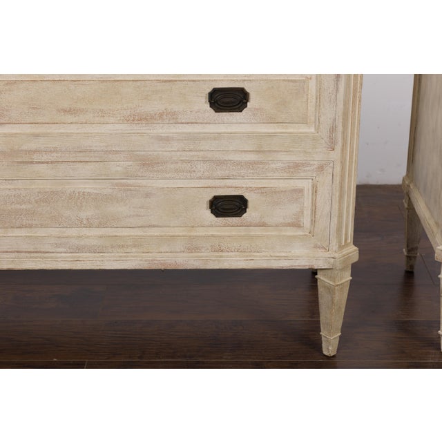 A pair of French Neoclassical style painted wood three-drawer chests from circa 1930 with light grey marble tops,...
