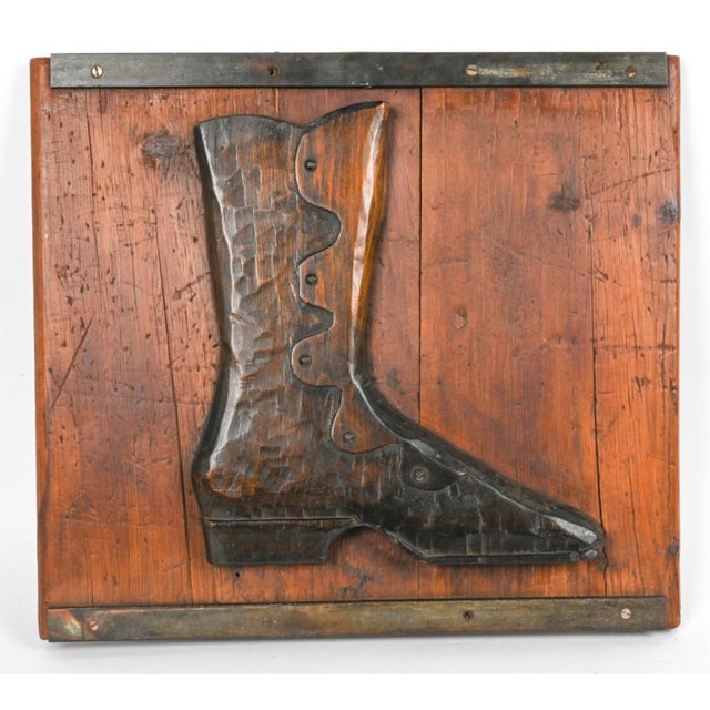 A vintage Victorian cobbler’s trade sign depicting a carved wooden relief of a high-buttoned boot mounted on a rustic pine...