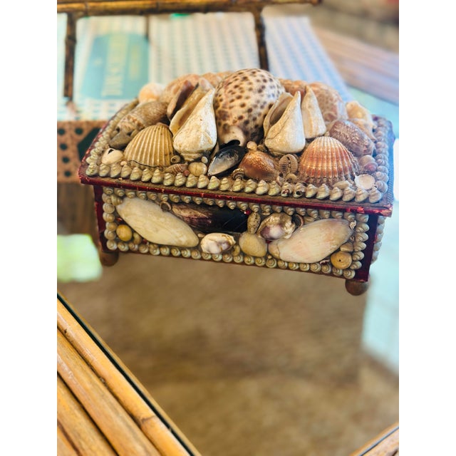 A charming antique wooden keepsake box beautifully adorned with an assortment of natural seashells, including cowries,...