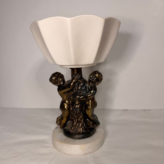 Ornate vintage Italian pedestal bowl features a pair of bronze-tone cherubs or cheribum or putti figures supporting a...