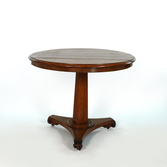 A round fruitwood center table with a plank-built top and molded edge above a plain frieze. The top is raised on a faceted...