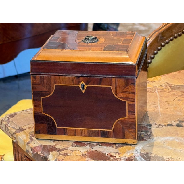 Inlaid tea caddy of canted rectangular form, the hinged lid and front centered with reserves bordered by stringing and...