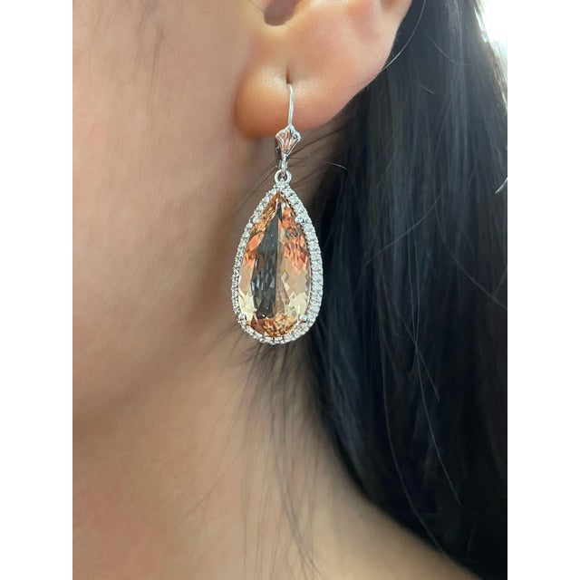 Elegant earrings featuring two pear-shaped natural morganites totaling 15.73 ct, each surrounded by 74 round brilliant...
