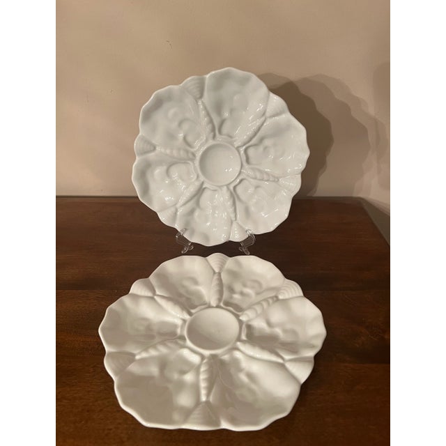 Two white porcelain German oyster plates with six wells, a center well for dipping or lemon in a seashell motif.