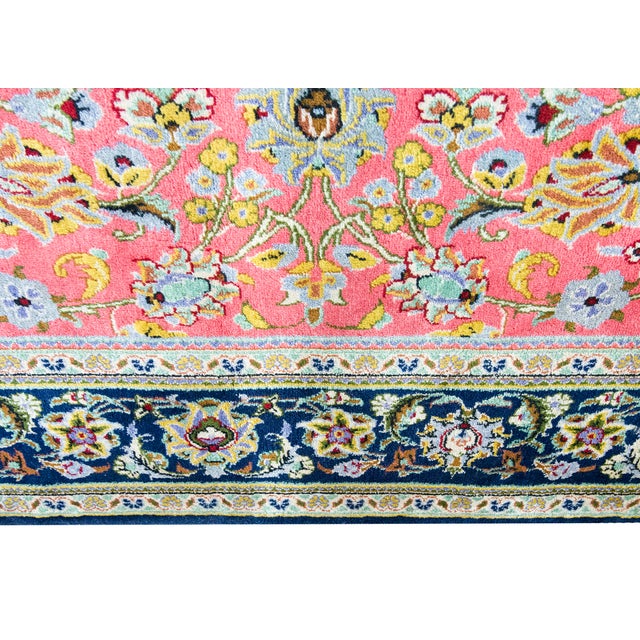 This hand-woven Persian Qum rug features a vibrant pink field adorned with intricate floral arabesques and scrolling vine...