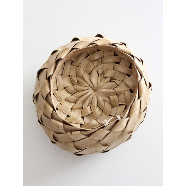 This vintage hand-woven palm frond basket features a round bowl shape and a bold geometric weave. The natural texture and...
