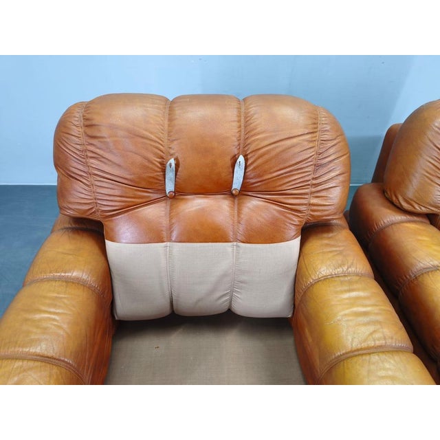 Pair of mid-century lounge armchairs produced in Italy during the 1970s. The armchairs are upholstered in cognac leather...