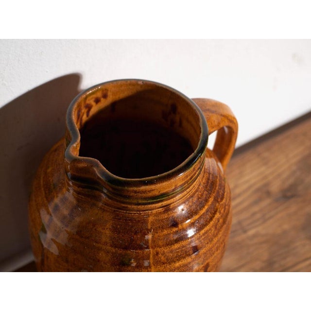 This antique folk glazed pottery jug is a spouted jug with a mottled amber glaze and a side handle . It originates from...