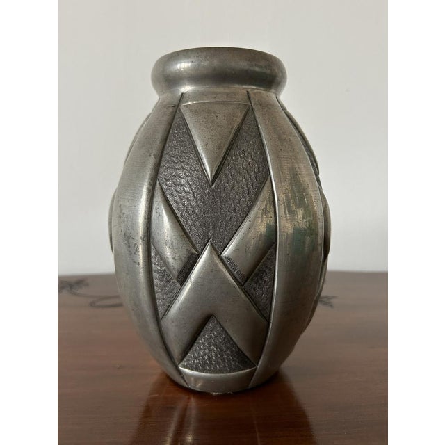 Hammered pewter vase, oval in shape, with raised geometric decorations and a distinctive hammered finish. The shapes...
