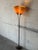 This striking floor lamp features a slender dark metal stem branching into dual adjustable arms with textured cone shades....