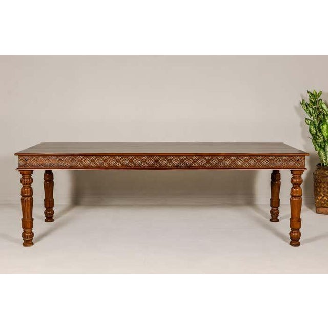 A large vintage dining table with carved apron showcasing floral motifs standing out on more unvarnished accents. This...