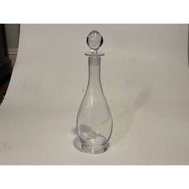 A curated pair of mid-century modern clear glass decanters featuring complementary geometric and organic silhouettes. The...