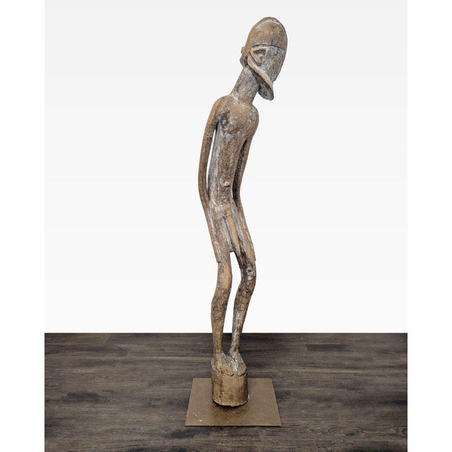 This is a unique hand-carved wooden sculpture featuring a slim, elongated figure with detailed facial features and a...