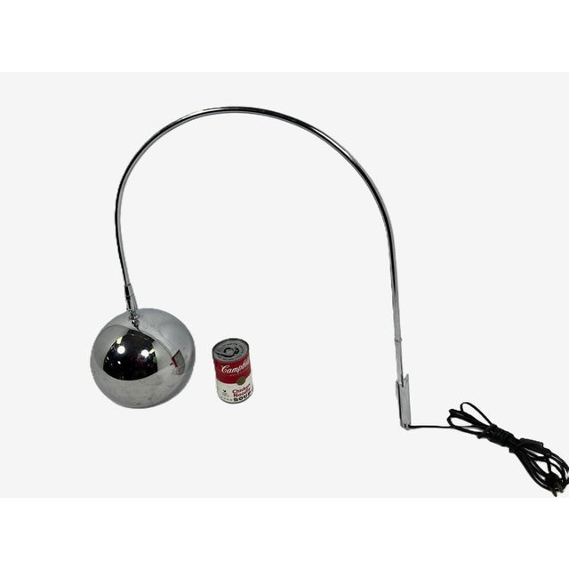 A chrome arc-shaped wall lamp with bracket designed by Robert Sonneman in the 1970's. A chrome ball-shaped shade hold a...
