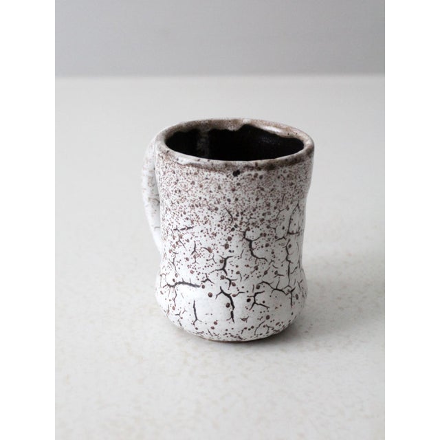 This vintage handmade studio pottery mug features a softly contoured form finished in a speckled white glaze with fine...
