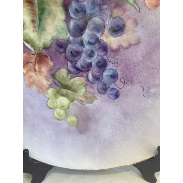 A captivating example of early 20th-century artistry, this hand-painted porcelain plate showcases lush grape clusters in...