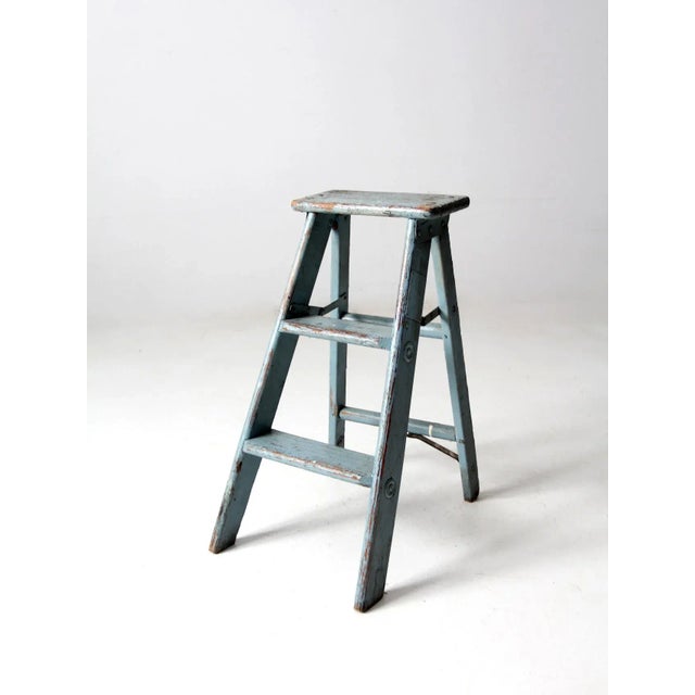 This vintage wooden step ladder features a compact two-rung form with beautifully aged sky-blue paint and a naturally...