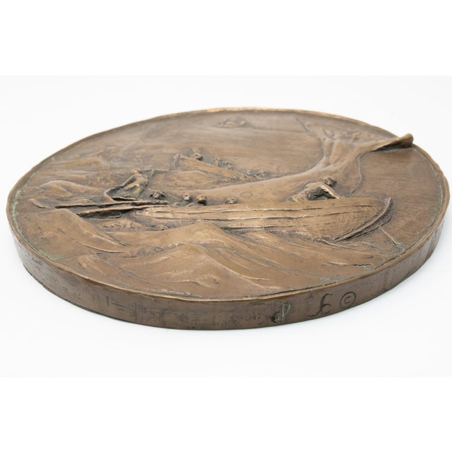 The wall plaque depicts three row boats in the midst of a whale. Off in the distance is a ship. People on board the row...