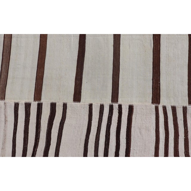 This flat-weave tribal Turkish kilim has been hand-woven in wool. The rug features an all-over sub-geometric striped panel...