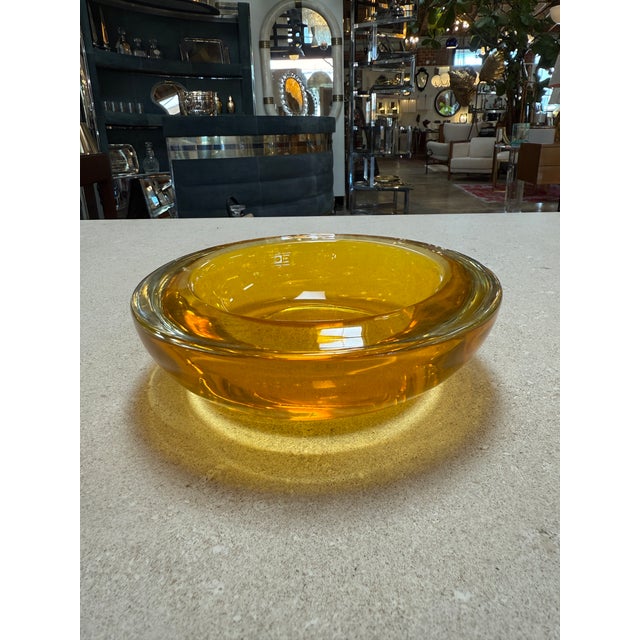 Vibrant hand-blown Murano glass bowl in a rich yellow tone. The piece features a wide, sculpted rim and a deep, smooth...
