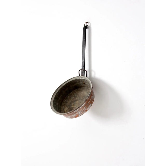 An antique hammered copper saucepan showcasing timeless craftsmanship and functional design. This piece features a warm,...