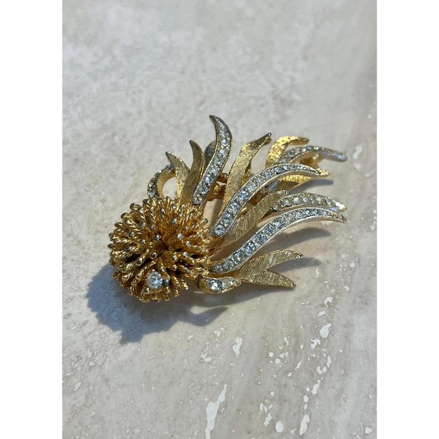 This vintage brooch takes the dramatic form of a dandelion or thistle bloom caught mid-burst, its densely textured gold-...