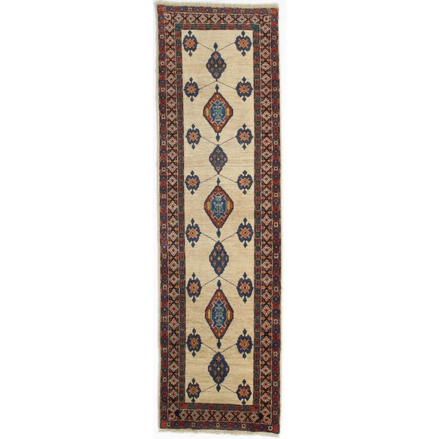 Vintage hand-knotted Persian Lori wool runner with an ivory field featuring repeating geometric medallions connected along...