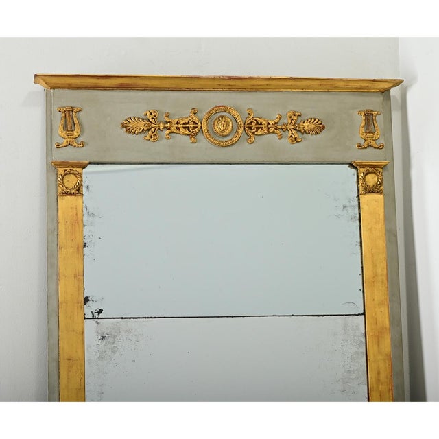A large 19th century French Empire trumeau mirror that is bold yet refined, using Neoclassical decorative elements to...