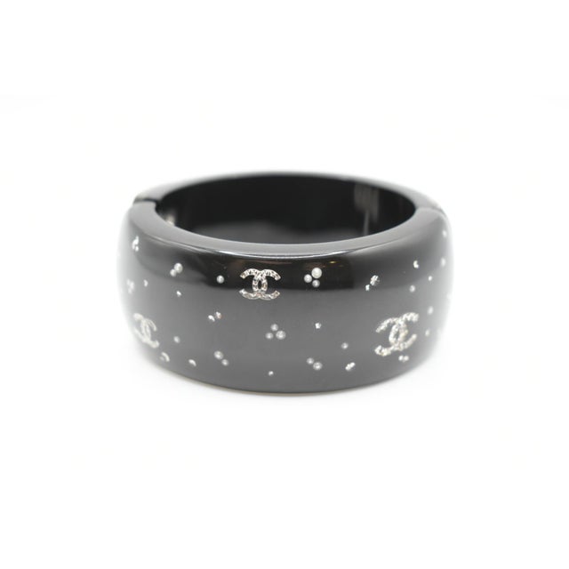 This is an amazing Chanel bangle. It is black resin with rhinestone crystal coco logos. The bangle has a hinged closure....