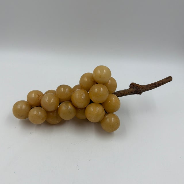 A sculptural cluster of vintage alabaster grapes in warm honey and golden tones, arranged on a natural wood branch stem....