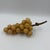 A sculptural cluster of vintage alabaster grapes in warm honey and golden tones, arranged on a natural wood branch stem....