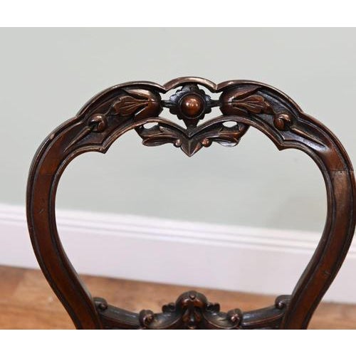 Elegant pair of Victorian salon chairs with shaped balloon backs and decorative carved details. The moulded back frames...