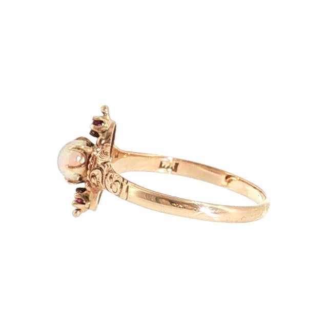 A Victorian 10K yellow gold opal and ruby ring. The opal is cut in a cabochon style, showcasing a mesmerizing blue, green,...