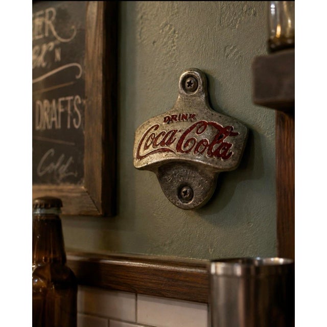 A classic vintage Coca-Cola “Drink Coca-Cola” STARR X wall-mounted bottle opener, rendered in cast metal with remnants of...