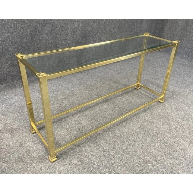 This brass and glass sofa table boasts a sleek, minimalist design, with a clear glass top that allows the elegant brass...