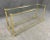 This brass and glass sofa table boasts a sleek, minimalist design, with a clear glass top that allows the elegant brass...