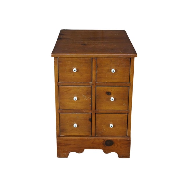 This mid-century apothecary chest is crafted from warm honey-toned pine, showcasing natural wood grains and prominent...