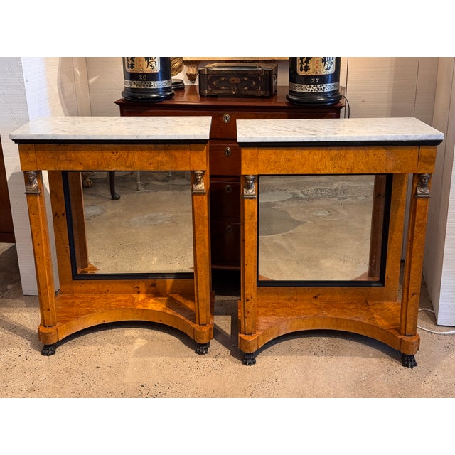 Empire-style pair of consoles with burlwood surfaces and white marble tops. Each console has a single drawer with visible...