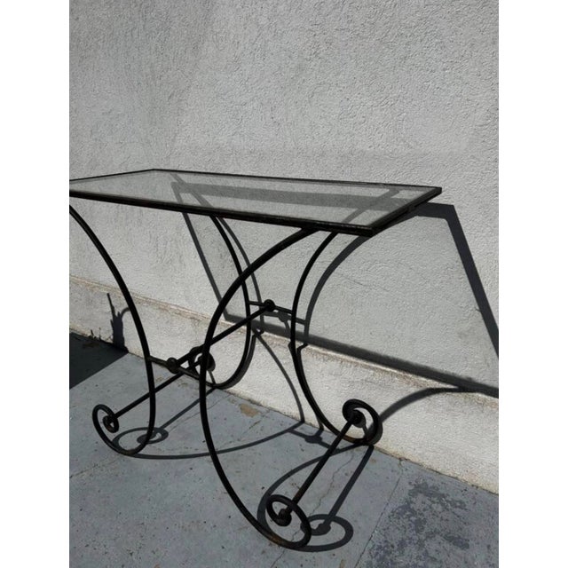 An elegant vintage wrought iron console table with a light, architectural silhouette composed of graphic curves and a...