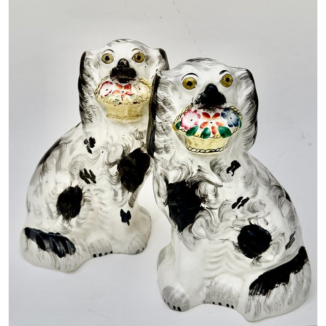 A charming and unusual pair of antique English Staffordshire spaniels, each seated upright and holding a flower filled...