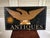 A hand-painted wooden trade sign with a golden folk art style eagle with outstretched wings gripping a globe, radiant sun...
