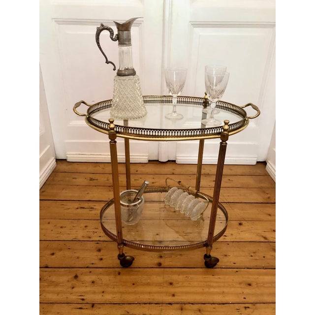 Elegant oval French Art Deco brass serving table with two glass shelves on casters, a removable top tray, and a beautiful...