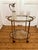 Elegant oval French Art Deco brass serving table with two glass shelves on casters, a removable top tray, and a beautiful...