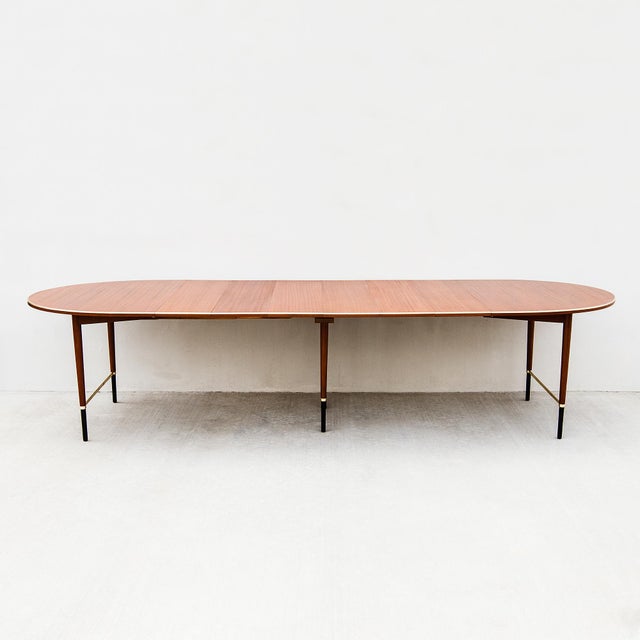 An outstanding expandable dining table in mahogany and brass with ebonized accents from Paul McCobb's Connoisseur...