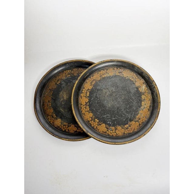 Pair of hand-painted, circular black trays adorned with a gilt floral frieze. The deep black background highlights the...