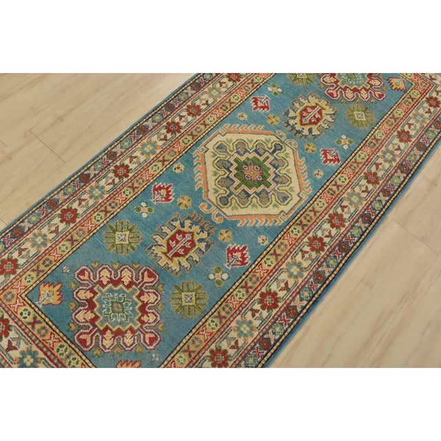 A tribal Caucasian Kazak runner hand-knotted with fine wool on a cotton foundation. This rug features geometric medallions...