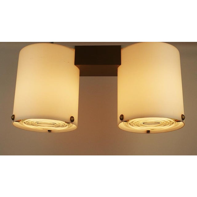 Ceiling lamp with two lighting connected by a varnished brass structure. The lighting is made up of two white satin glass...