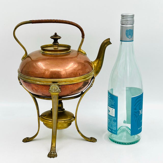 Antique copper kettle with brass spout, trim, handle, and lid, resting on a brass stand with wonderfully detailed lion...